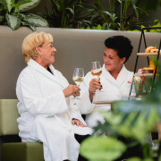 Twee dames in badjas proosten met een glas wijn bij wellness restaurant Bread & Bites.