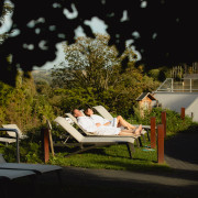 Koppel ligt in badjas te genieten van de zon op de ligweide met uitzicht over het limburgse heuvelland.