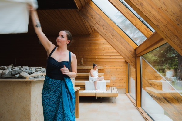 Saunameester verzorgt opgieting met handdoek in sauna met mooi uitzicht. 