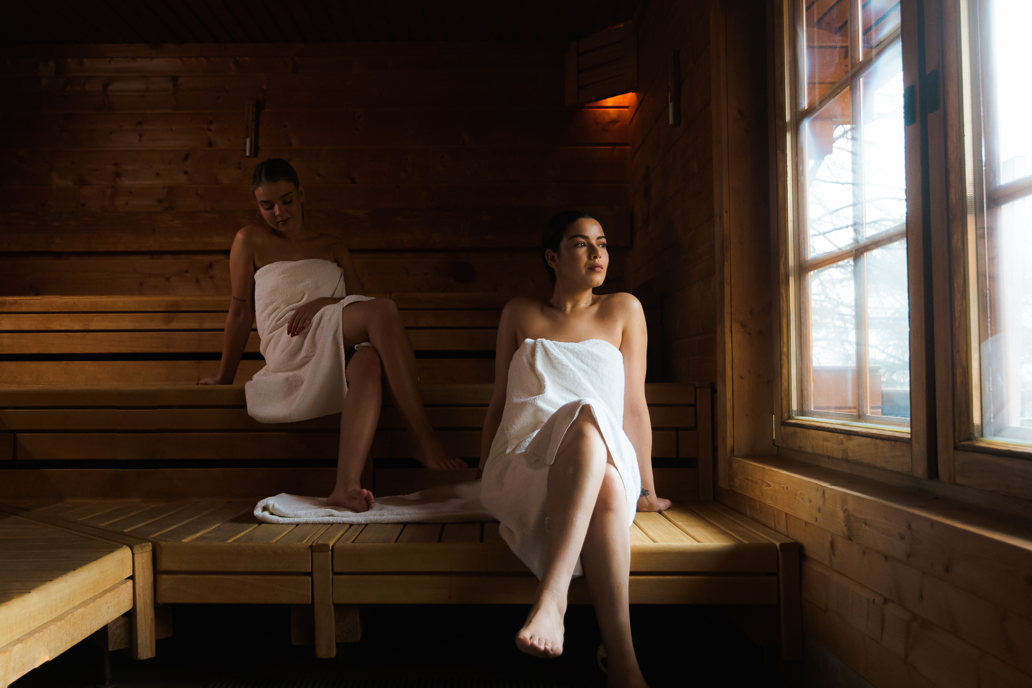 Twee dames ontspannen in handdoek in buitensauna Suola en kijken uit het raam.