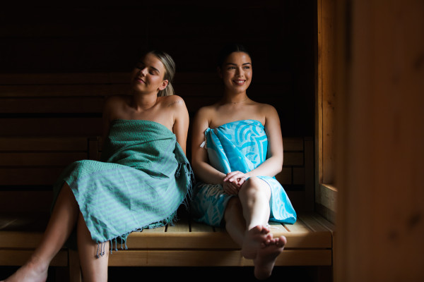 Twee dames in blauwe hammamdoek genieten in de Stuga sauna.